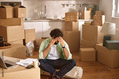 Fotografie A person sits on the floor among unpacked boxes, displaying frustration while trying to manage the chaos of a recent move