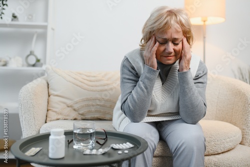 Senior woman sitting on a sofa at home with a headache, feeling pain and with an expression of being unwell