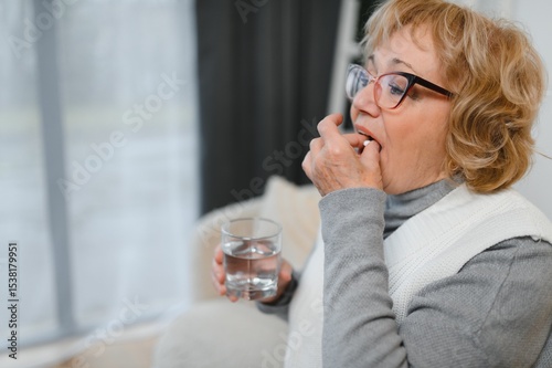Senior woman at home sitting at home holding cup of water and pill