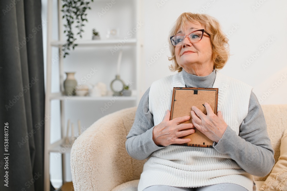 Photo of attractive aged woman look photo frame nostalgia remember sit couch home Photo of attractive aged woman look photo frame nostalgia remember sit couch home