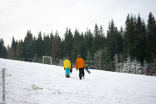 Enjoying a winter adventure together on a snowy slope while heading for some fun snowboarding near a group of evergreen trees