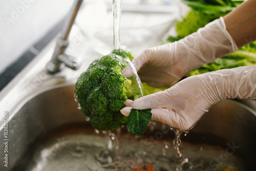 Woman washing fresh vegetables at kitchen sink, practicing hygiene and food safety indoors to prevent illness during pandemic, ensuring healthy lifestyle and cleanliness.