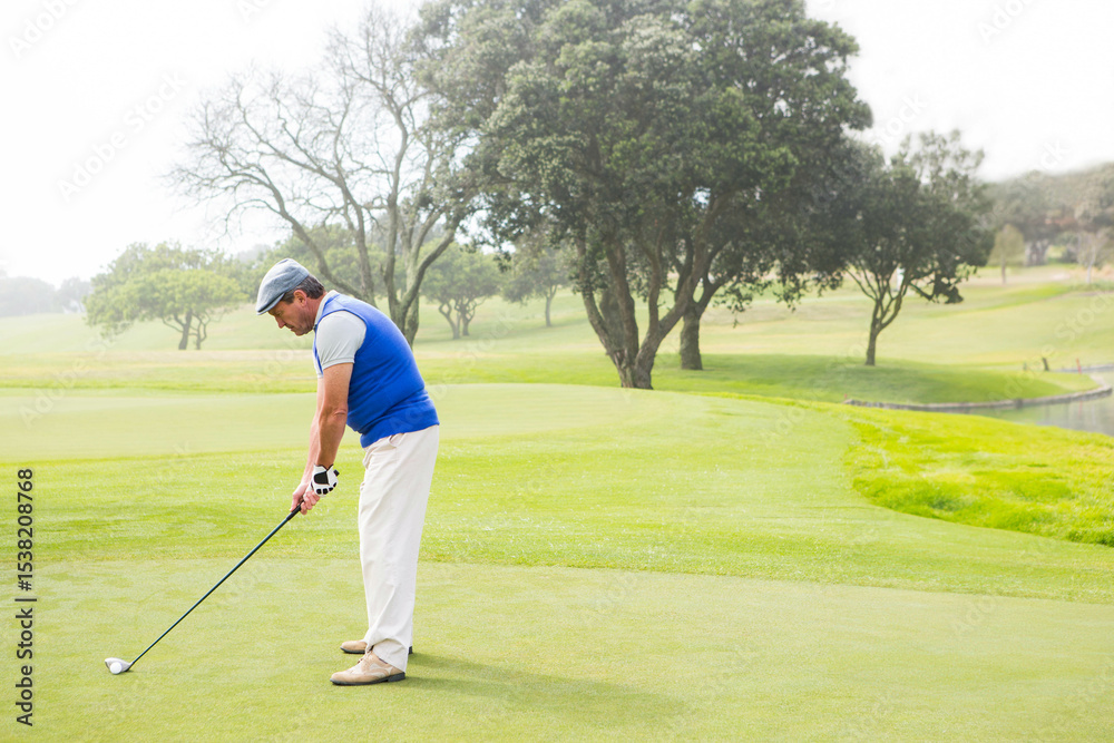 Fototapeta premium Senior male golfer standing on trimmed fairway near pond wearing golf glove and gripping club