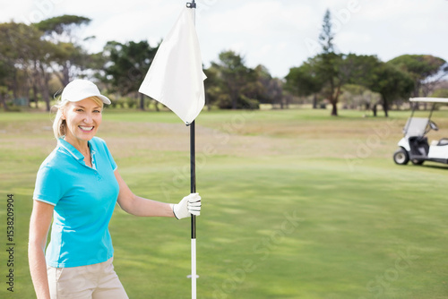 Woman holding white flagstick on putting green, golf hole, golf glove, golf cart, copy space