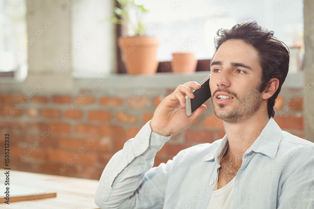 Male holding smartphone to ear while sitting at table by brick wall windowsill with terracotta pots Male holding smartphone to ear while sitting at table by brick wall windowsill with terracotta pots