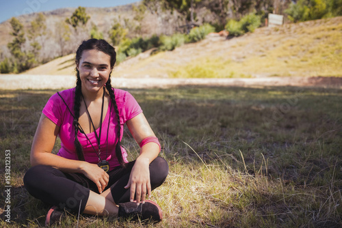 woman in her twenties sitting crosslegged in meadow wearing sweatband holding whistle near sneakers