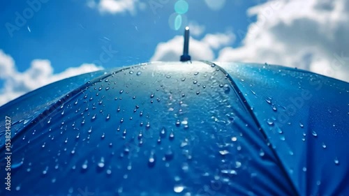 Rain drops accumulate on a vibrant blue umbrella beneath a bright sky with clouds during daytime	