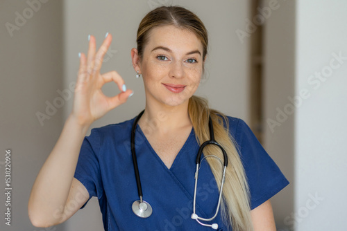 Confident medical professional showing okay hand sign wearing stethoscope and scrubs