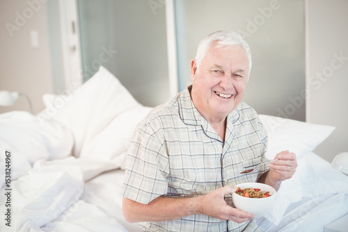 bowl holding granola and fruit resting on bed with pillows and lamp near frosted glass doors