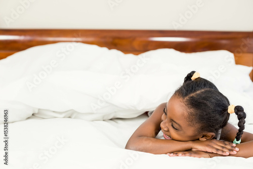 African American child lying on bed smiling amid white pillows and duvet in bedroom, copy space