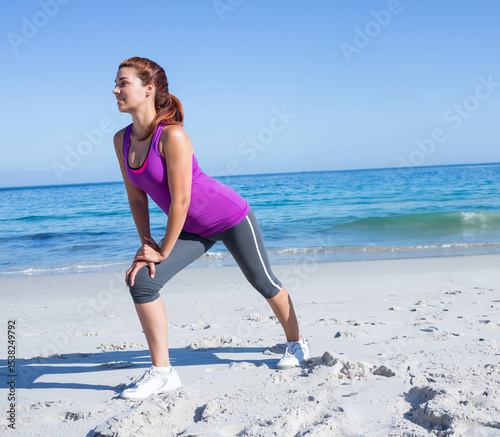 Woman in sportswear doing lateral lunge stretch on white sandy beach under blue sky, copy space