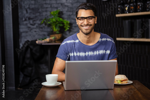 Laptop sitting on wooden table at casual cafe interior, with coffee cup and sandwich