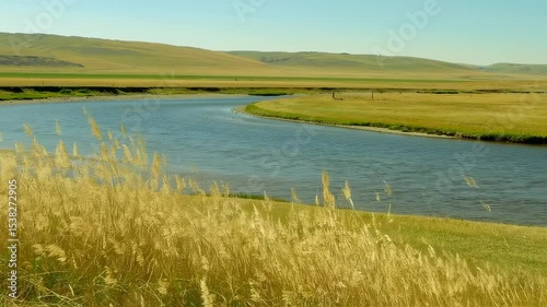 Scenic river flowing through vast grasslands with rolling hills in the distance