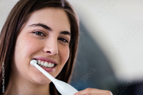 Woman brushing teeth with white electric toothbrush in bathroom near mirror wearing light top