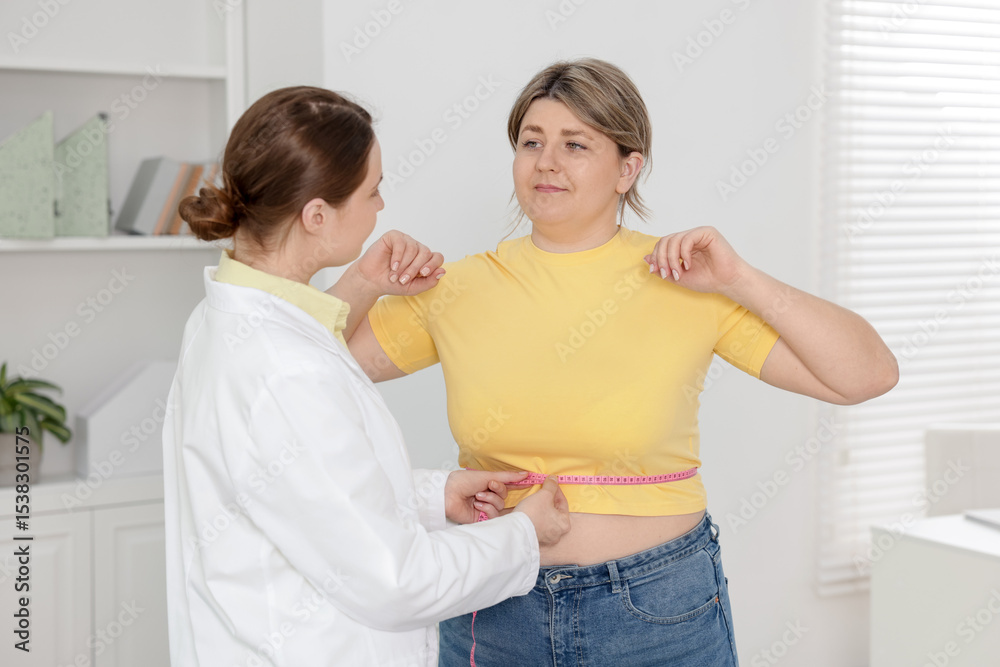 Fototapeta premium Weight loss. Nutritionist measuring overweight woman's waist with tape in clinic