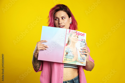 Photography Beautiful woman with pink dyed hair holding sports magazine on yellow background