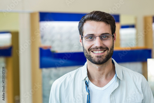 Man standing in optical store wearing denim shirt and metal frame eyeglasses near display shelves photo