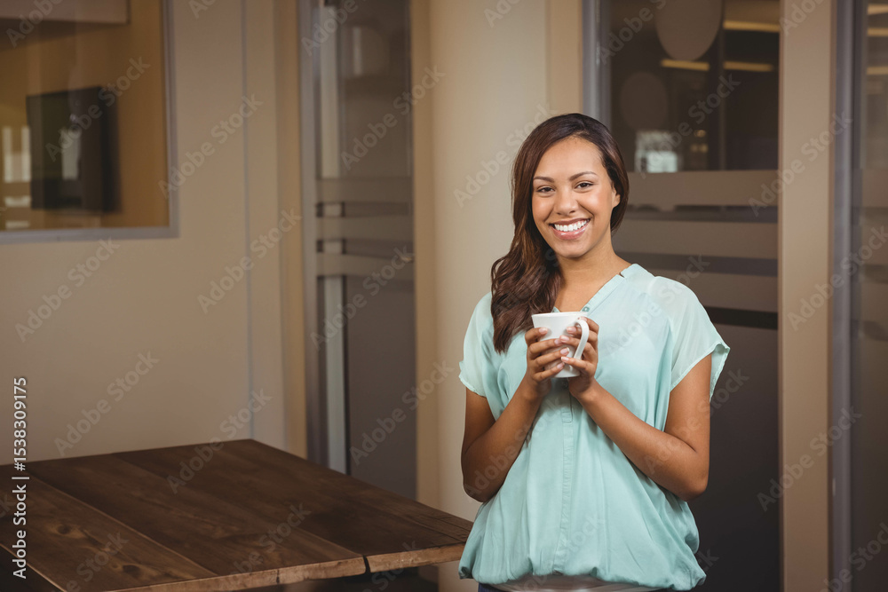 African American woman in mint green blouse standing in breakroom holding white mug, copy space African American woman in mint green blouse standing in breakroom holding white mug, copy space