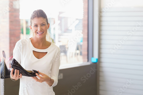 Woman holding glossy black patent leather high heel at shoe store counter with handbag, copy space photo