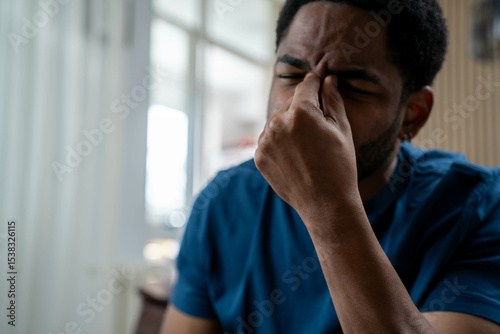 Young African American man holding head in pain at home living room, migraine and headache discomfort, feeling unwell and stressed during daytime