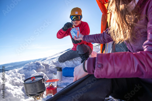 Couple rehydrating freeze-dried meal at snowy mountain campsite. Winter tent, camping stove, outdoor gear and alpine cooking in cold weather