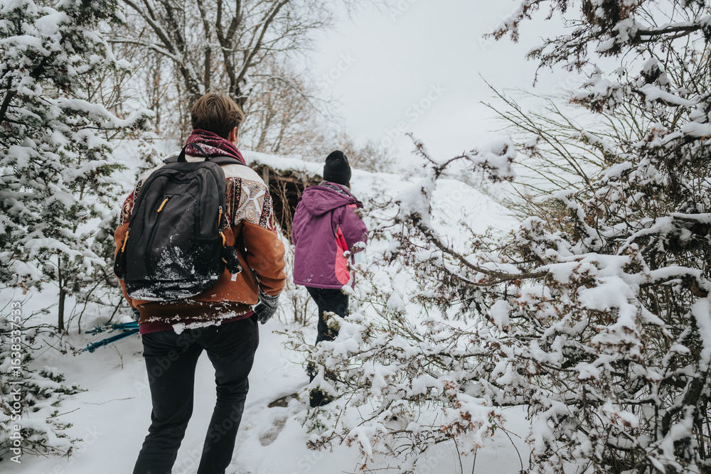 Naklejka premium Two people hiking along a snowy forest trail surrounded by trees covered in fresh snow, experiencing the serene outdoors.