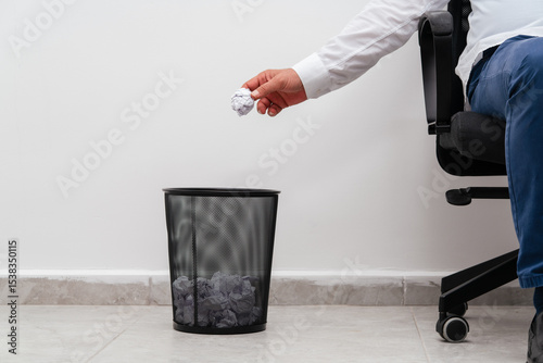 A man in office throwing a paper into the trash bin