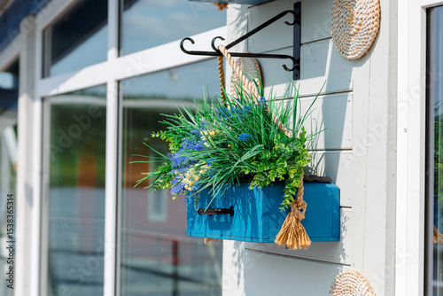Tableau sur toile A bright blue flower box, suspended from a metal hook, is decorated with greenery and flowers, creating a cozy and stylish accent on the facade