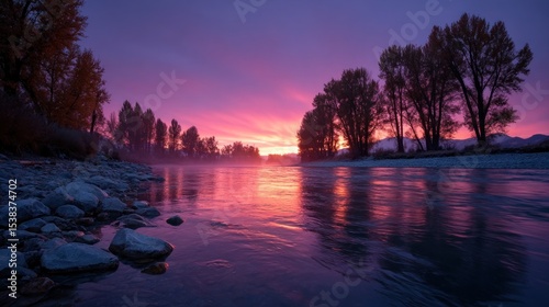 stunning sunset paints the sky in shades of purple and orange over a calm river. Silhouetted trees stand along the banks, creating a peaceful atmosphere in the early evening