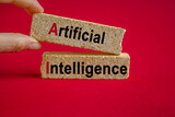 Brick blocks form the text 'AI - artificial intelligence' on beautiful red background. Businessman hand. Business concept