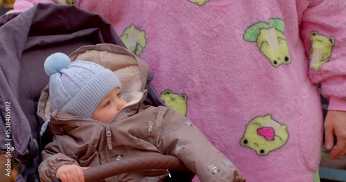 A loving father gently interacts with his adorable baby, who is snugly dressed in warm winter attire, while they enjoy the fresh air next to a stroller in the lovely park