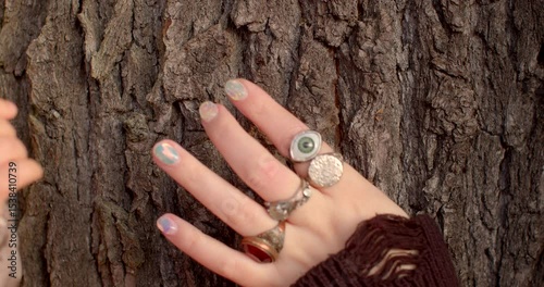 Two hands are engaging with the rough, textured bark of a tree, beautifully displaying various pieces of jewelry, including several rings, while a small childs hand curiously reaches out