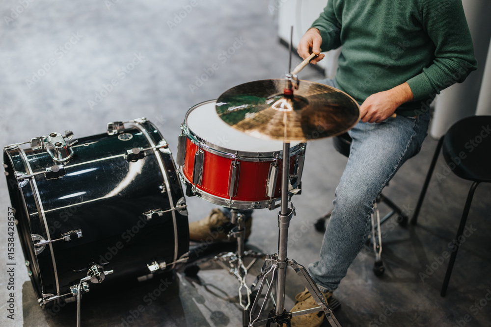 A person in a green sweater and jeans plays the drums with focus and skill indoors. The image captures the essence of music practice and dedication, highlighting the musician's relaxed style. A person in a green sweater and jeans plays the drums with focus and skill indoors. The image captures the essence of music practice and dedication, highlighting the musician's relaxed style.