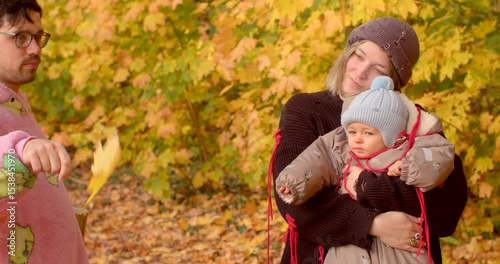 A joyful family enjoys vibrant autumn scenery, with a baby in a carrier surrounded by colorful leaves, capturing the essence of fun outdoor activities in this lovely season