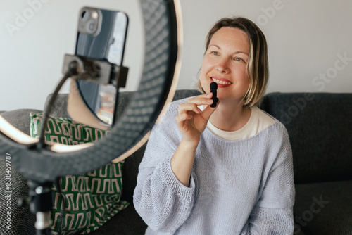 Middle-aged woman beauty blogger filming skincare product unboxing at home with ring light. User-generated content UGC for online store promotion. Vlogger live streaming. Part of a series