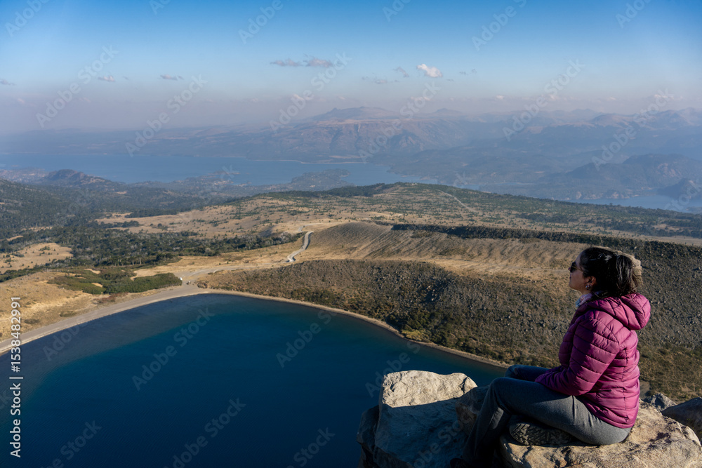 Naklejka premium Woman sitting on rock with scenic view from Batea Mahuida and Alumine Lake. Villa Pehuenia, Neuquen, Argentina
