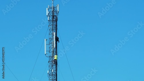 Two workmen on a cell tower. Maintenance staff at the work. High-altitude work. Cell tower on blue background. Repairmen service a cell tower, install new equipment