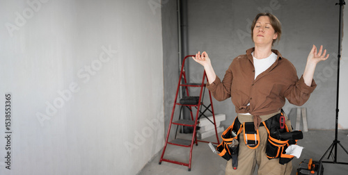 relaxed young repairwoman makes zen gesture. Female handywoman meditates indoor doing house repair practices yoga