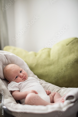 Infant boy reclining in baby lounger wearing white onesie on sofa with green cushion, copy space