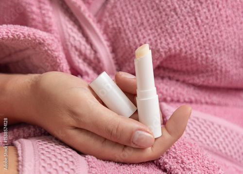 Woman in pink bathrobe holding in hand opened lip balm stick with a lid closeup, girly mockup