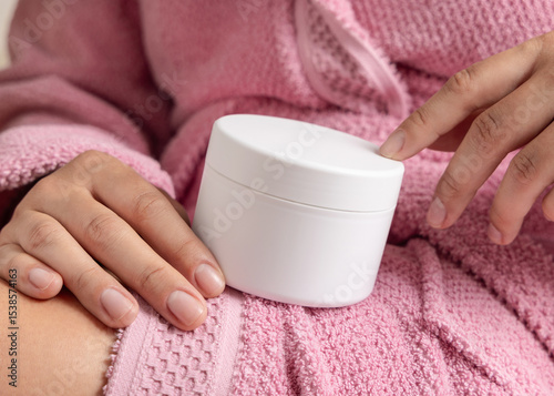 Closeup of young  woman in pink bathrobe holding white cream jar in hands, cosmetic mockup