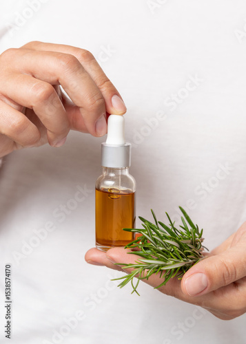 Closeup of female hands holding small dropper oil bottle and fresh rosemary sprigs