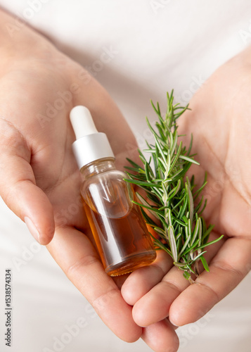 Closeup of female hands holding small dropper oil bottle and fresh rosemary sprigs, herbal medicine
