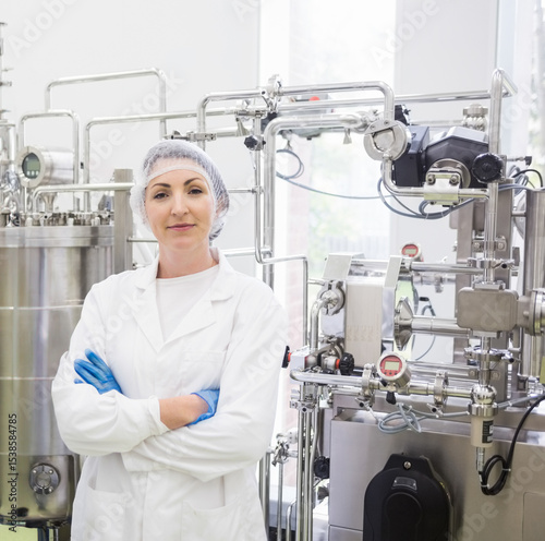 Woman in lab coat hair net blue gloves standing beside stainless mixing tank at processing plant