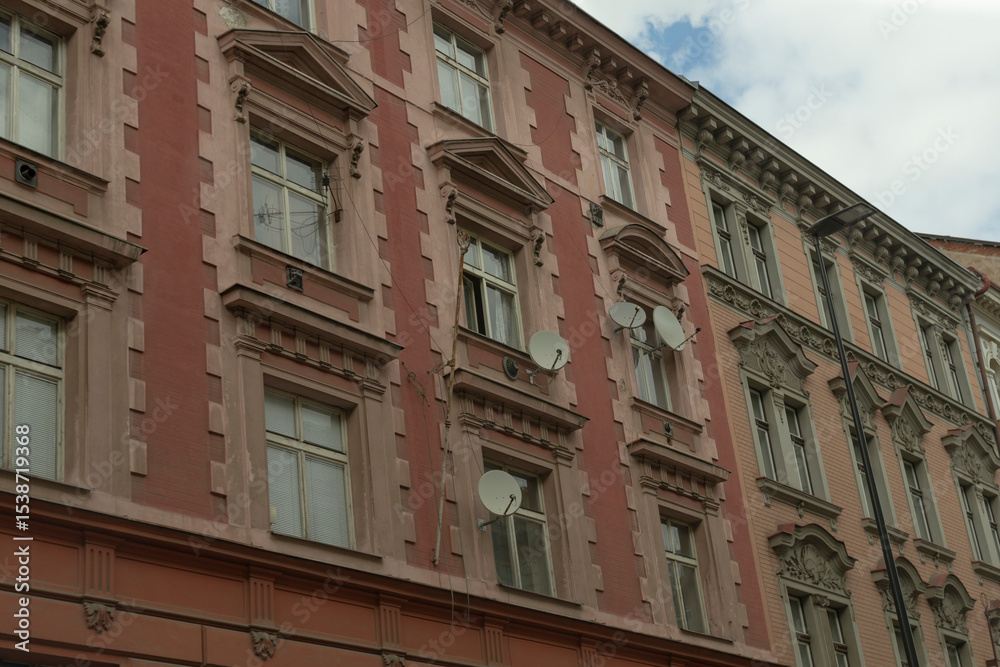 Fototapeta premium The facade of a wellpreserved historical building showcases numerous charming windows, intricate architectural details, and modern satellite dishes set against a bustling urban environment