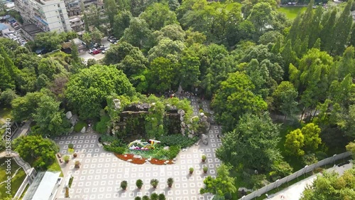 Aerial view shows lush trees, decorative waterfall, and floral display in Chengdu Peoples Park, China