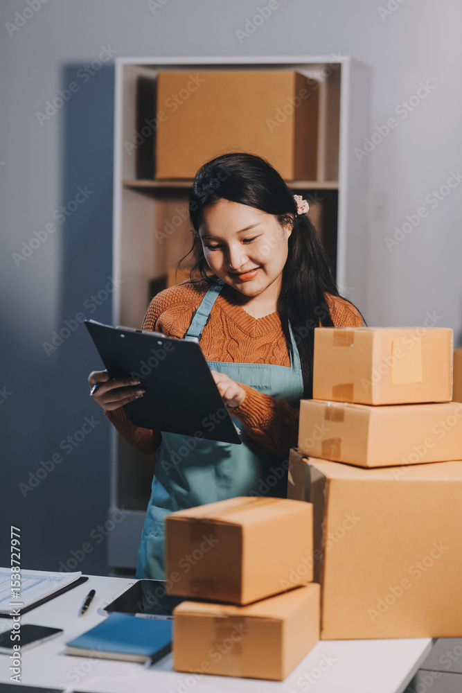 Startup SME small business entrepreneur of freelance Asian woman wearing apron using laptop and box to receive and review orders online to prepare to pack sell to customers, online sme business ideas. Startup SME small business entrepreneur of freelance Asian woman wearing apron using laptop and box to receive and review orders online to prepare to pack sell to customers, online sme business ideas.