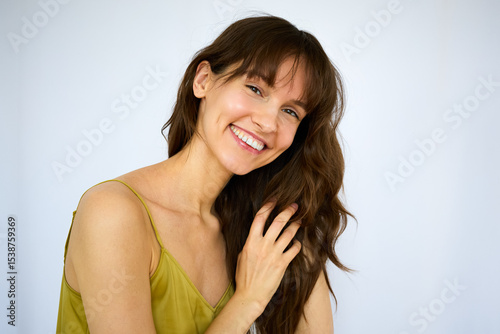 Beautiful happy playful brunette with the big smile holding her beautiful long thick hair on the white background