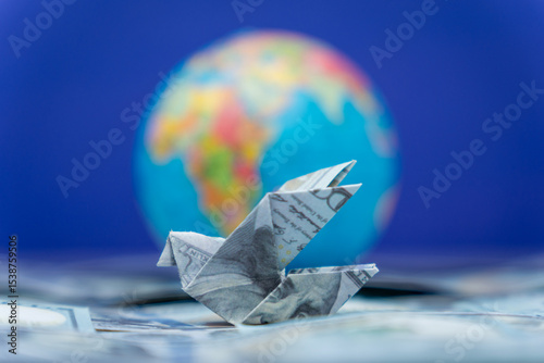 An origami bird folded from a US dollar bill and a globe. International financial transfers, remittances, and global money movement concept.