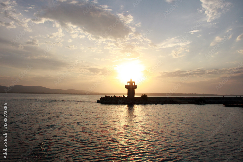 Lighthouse on a stone breakwater silhouetted against a golden sunset sky. Lighthouse on a stone breakwater silhouetted against a golden sunset sky.